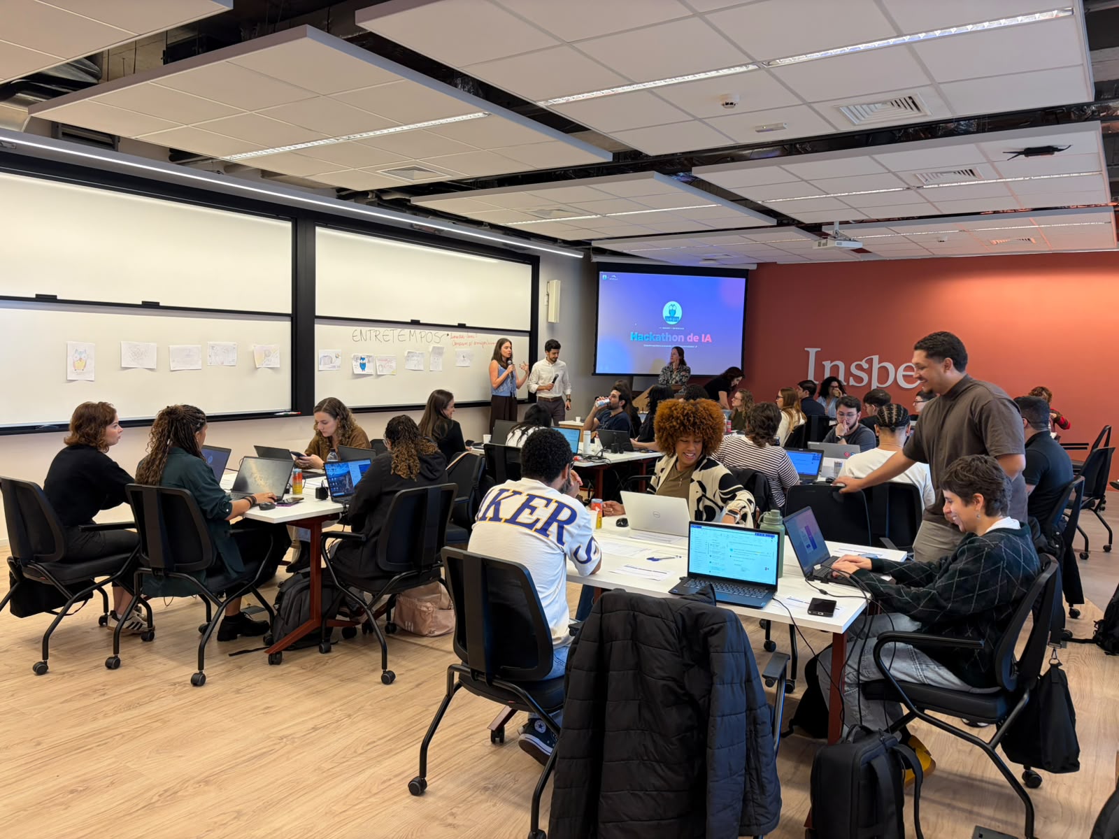 Vista ampla da sala do hackathon de IA no Ismart com dezenas de pessoas trabalhando em times